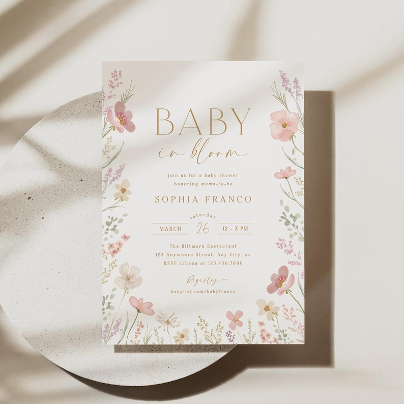 May include: A baby shower invitation with a floral design. The invitation is white with pink and purple flowers and greenery. The text on the invitation reads "Baby in Bloom", "Sophia Franco", "March 26", "12-3 PM", "The Biltmore Restaurant", "123 Anywhern Street, Any City, as", "RSVP Liliana at 123.456.7800", "Registry", "babylist.com/babyfranco".