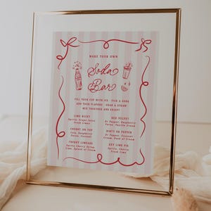 May include: A framed pink and white sign with a gold border, advertising a soda bar. The sign features red text and illustrations, including soda bottles and glasses. It lists soda flavor combinations like Lime Ricky and Cherry Limeade.