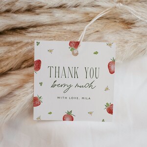 May include: Square gift tag with a strawberry theme. The tag features the text "THANK YOU berry much" in green script and block letters, with the name "MILA" below. Watercolor strawberries and small white flowers are scattered across the white background.