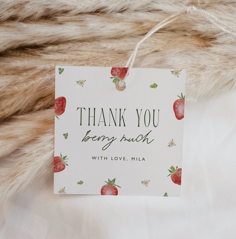 May include: Square gift tag with a strawberry theme. The tag features the text "THANK YOU berry much" in green script and block letters, with the name "MILA" below. Watercolor strawberries and small white flowers are scattered across the white background.