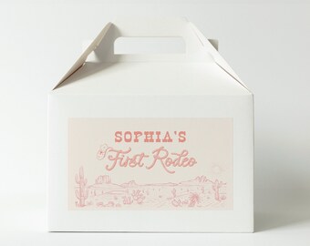 May include: White cardboard box with a handle. The box has a pink label with the text "Sophia's First Rodeo" and a drawing of a desert landscape with cacti.