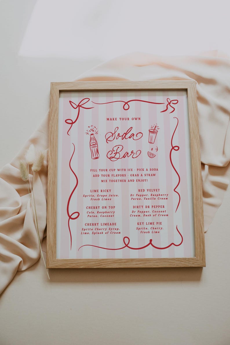 May include: A framed sign with a pink and white striped background and red text that reads "Make Your Own Soda Bar." The sign lists soda flavor combinations like Lime Ricky and Cherry on Top. The frame is made of light-colored wood.