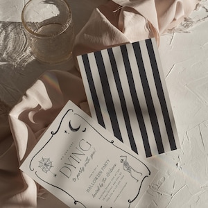 May include: Halloween party invitations with a black and white striped card and a clear glass. The invitation reads "DYING to party with you!" with a skeleton illustration and event details. The background includes a beige fabric.