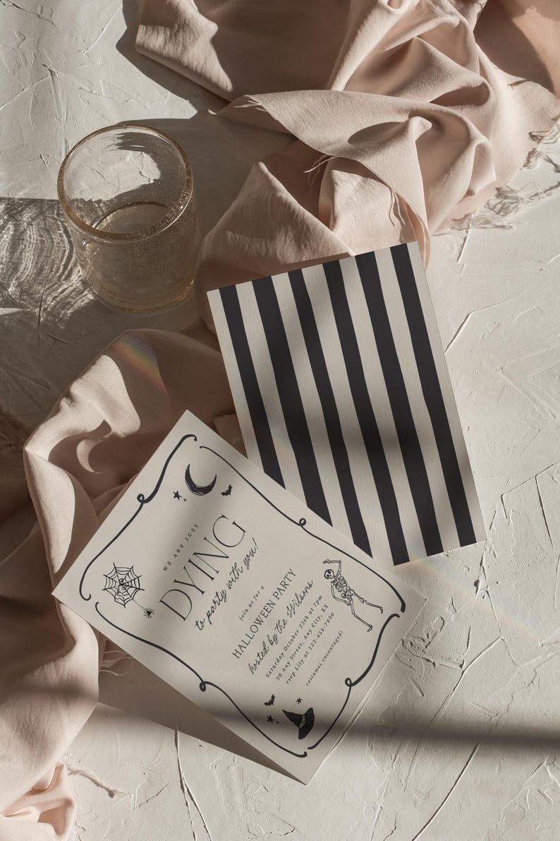 May include: Halloween party invitations with a black and white striped card and a clear glass. The invitation reads "DYING to party with you!" with a skeleton illustration and event details. The background includes a beige fabric.