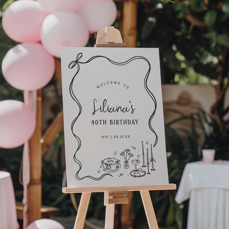 May include: A white sign on a wooden easel with the text "Welcome to Liliana's 40th Birthday" in black script. The sign is decorated with a black line border and illustrations of party elements. Pink balloons are visible in the background.