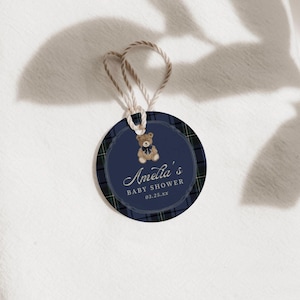 Può includere: Tag rotondo per baby shower con sfondo blu navy e bordo a quadri. Il tag presenta un'illustrazione di orsetto e il testo "Amelia's Baby Shower" con la data 03.25.xx. È attaccato un anello di spago naturale.