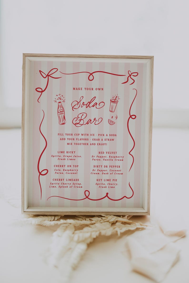 May include: A framed sign with a pink and white striped background and red text. The sign reads "Make Your Own Soda Bar" and lists soda flavor combinations like Lime Ricky and Red Velvet. Decorative red swirls and bows frame the text.
