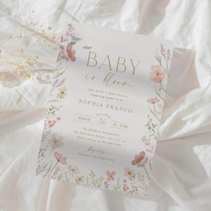 May include: A baby shower invitation with a floral design. The invitation reads "Baby in Bloom" and includes the name "Sophia Franco" and the date "March 26".