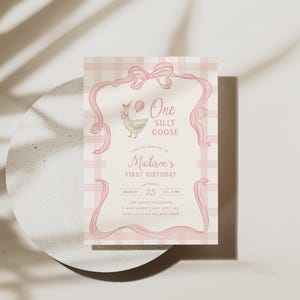 May include: A pink and white invitation card with the text "One Silly Goose" and "Madison's First Birthday." The card features a cartoon goose holding a balloon and is decorated with pink ribbons and a plaid background.