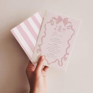 以下が含まれることがあります： ピンク色のメニューカード。リボンのデザインと筆記体で書かれた「Menu」の文字が特徴です。メニューには前菜、メイン、デザートが記載されています。カードの裏面はピンクと白のストライプです。