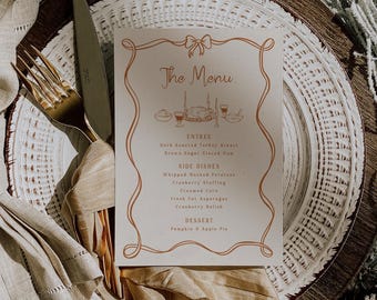 May include: A rectangular menu card with a copper-colored ribbon border and a central illustration of a holiday feast. The text reads The Menu, Entree, Herb Roasted Turkey Breast, Brown Sugar Glazed Ham, Side Dishes, Whipped Mashed Potatoes, Cranberry Stuffing, Creamed Corn, Fresh Cut Asparagus, Cranberry Relish, Dessert, and Pumpkin & Apple Pie.