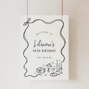 May include: A black and white birthday sign with the text "Welcome to Liliana's 40th Birthday." The sign includes decorative line art of a ribbon, cake, flowers, candles, and a cocktail glass. The location and date are also included.