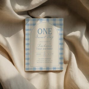May include: A light blue and white gingham patterned invitation card. The text reads "ONE Sweet Boy" and "Jackson's FIRST BIRTHDAY". The invitation includes the date, time, and location for the event.