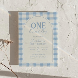 Może przedstawiać: Niebiesko-biała karta zaproszenia w kratę. Tekst brzmi "ONE Sweet Boy" i "Jackson's FIRST BIRTHDAY", z datą, godziną i adresem. Projekt zawiera łukowatą ramę i niebieską kolorystykę.
