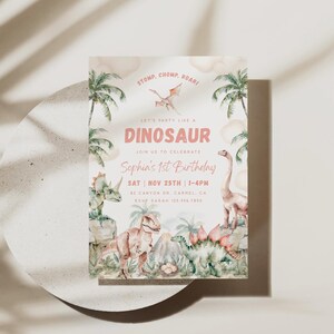 May include: A pink and green dinosaur-themed first birthday party invitation with a watercolour background. The invitation features a variety of dinosaurs, including a T-Rex, a stegosaurus, and a pterodactyl. The text on the invitation reads "Let's party like a dinosaur, join us to celebrate Sophia's 1st birthday, Sat Nov 25th 1-4pm, 82 Canyon Dr. Carmel, CA, RSVP Sarah 123.456.7850."
