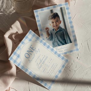 May include: Two invitations with a blue and white gingham border. One features a photo of a smiling child. The other says "ONE Sweet Boy" and "Jackson's FIRST BIRTHDAY" with the date and time. The invitations are on a white textured surface.