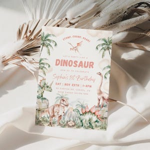 May include: A pink and green dinosaur-themed first birthday party invitation with a watercolour illustration of dinosaurs, palm trees, and a volcano. The text reads "Stomp, Chomp, Roari Let's Party Like a Dinosaur Join Us to Celebrate Sophia's 1st Birthday Sat | Nov 25th | 1-4pm 32 Canyon Dr Carmel, CA RSVP Sarah 122.456.7890"