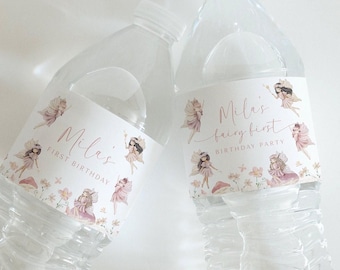 Peut inclure: Deux bouteilles d'eau en plastique transparent avec des étiquettes blanches illustrées de fées, de fleurs et de champignons. Le texte indique Mila's First Birthday et Mila's Fairy First Birthday Party en lettres cursives et capitales.