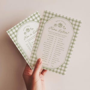 May include: Two rectangular game cards with a sage green and white gingham border. The cards feature decorative line art of a picnic basket and fruit. One card is titled "Guess Who Mom or Dad" and the other is titled "What Would Mama Rather?" with a list of choices.