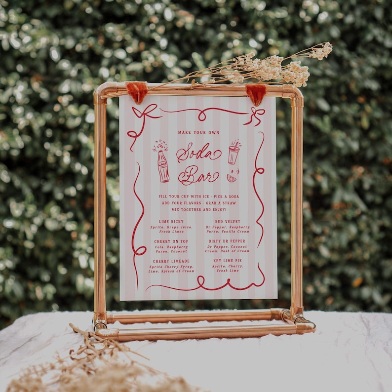 May include: A copper-colored metal frame holds a sign for a soda bar. The sign has a red and white striped background with red text and illustrations. The text reads "Make Your Own Soda Bar" and lists soda flavor combinations.
