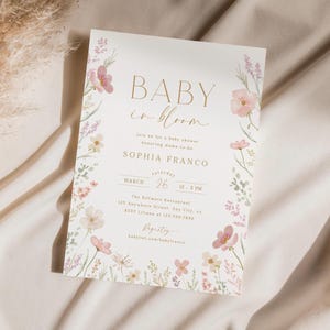 May include: A baby shower invitation with a floral design. The invitation is white with gold lettering and says "Baby in Bloom" and "Sophia Franco". The date is March 26th and the time is 12-3 PM. The location is The Biltmore Restaurant, 123 Anywhere Street, Any City, s. The RSVP number is 123.456.7890. The registry is babylist.com/babyfranco.