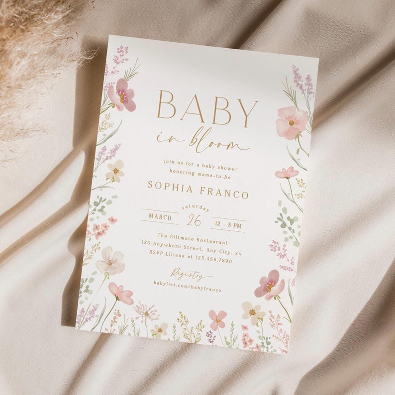 May include: A baby shower invitation with a floral design. The invitation is white with gold lettering and says "Baby in Bloom" and "Sophia Franco". The date is March 26th and the time is 12-3 PM. The location is The Biltmore Restaurant, 123 Anywhere Street, Any City, s. The RSVP number is 123.456.7890. The registry is babylist.com/babyfranco.