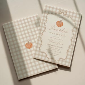 Puede incluir: Una invitación para baby shower con estampado de cuadros vichy en beige y blanco y su sobre a juego. La invitación presenta un marco festoneado central con una ilustración de calabaza en acuarela y el texto A LITTLE PUMPKIN IS ON THE WAY! para Olivia Grace.