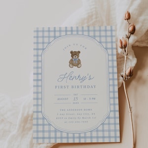 May include: A rectangular birthday invitation card featuring a light blue and white gingham pattern border. The center displays a brown teddy bear with a blue bow, the text Henry's FIRST BIRTHDAY, and event details including date, time, and location.