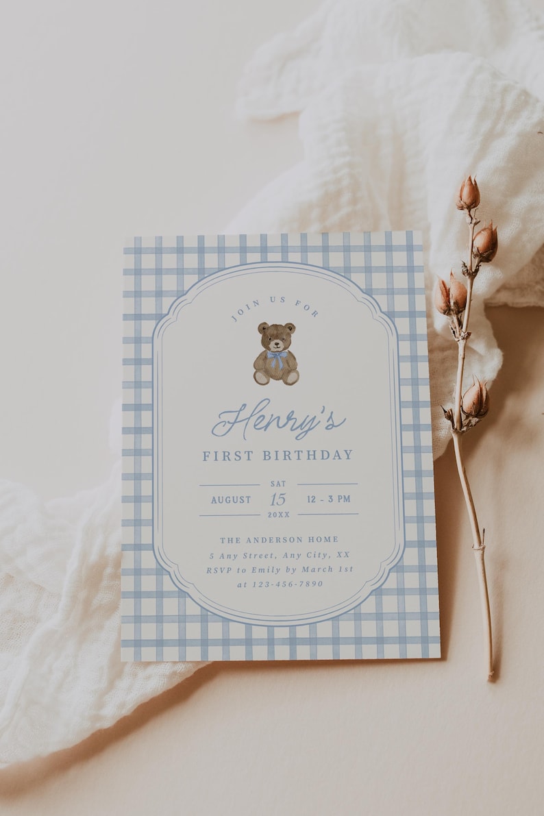 May include: A rectangular birthday invitation card featuring a light blue and white gingham pattern border. The center displays a brown teddy bear with a blue bow, the text Henry's FIRST BIRTHDAY, and event details including date, time, and location.