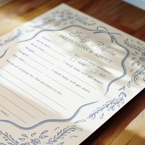 Pu&ograve; includere: Un biglietto per il gioco del baby shower color crema chiaro con il testo "Baby Robins Predictions & Advice" in elegante scrittura. La carta presenta un bordo floreale blu decorativo e spazio per le previsioni sul bambino.