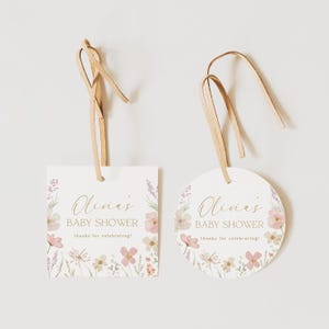 May include: Two baby shower favor tags with a floral design. One tag is square and the other is round. Both tags have the text "Olivia's Baby Shower thanks for celebrating!" in gold lettering.