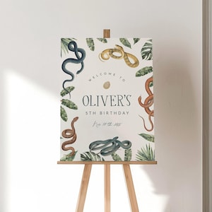 May include: A rectangular birthday welcome sign on a wooden easel featuring illustrations of various snakes and tropical leaves. The text reads: Welcome to Oliver's 5th Birthday Nov 10th 2024, with a small egg icon centered above the name.