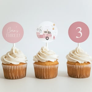 May include: Three pink and white cupcake toppers with a fire truck, the number 3, and the text "Clara's THREE!"