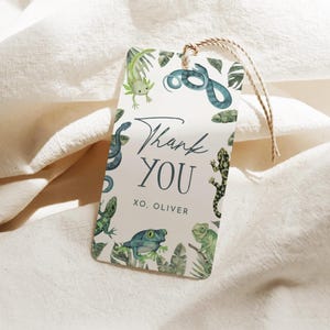 Puede incluir: Una etiqueta de regalo rectangular con un diseño de acuarela que presenta varios reptiles y el texto "Thank You XO, Oliver". La etiqueta está adornada con una cuerda de hilo para sujetar y está sobre un fondo blanco roto.