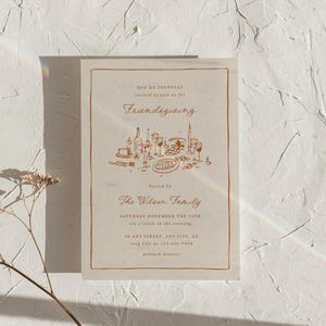 K&ouml;nnte beinhalten: Eine beige Friendsgiving-Einladung mit braunem Rand und Text. Die Einladung enth&auml;lt die W&ouml;rter "Friendsgiving" und "The Wilson Family". Eine detaillierte Illustration einer Tischdekoration mit Speisen und Getr&auml;nken ist ebenfalls vorhanden.