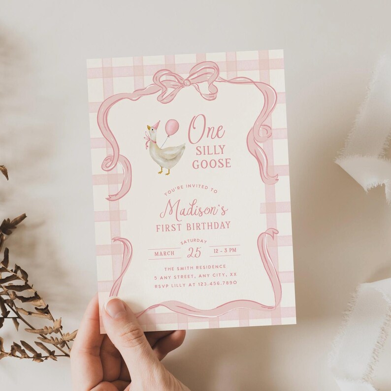 May include: A pink and white invitation card for a first birthday. The card features a cartoon goose holding a balloon, the text "One Silly Goose", and the name "Madison's". The card has a pink ribbon and gingham pattern.
