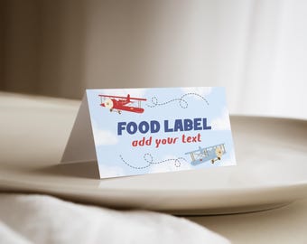 May include: A folded paper food label featuring a light blue sky background with white clouds, a red airplane, and a light blue airplane. The text reads FOOD LABEL and add your text in dark blue and red, with dashed flight paths.