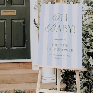 Pu&ograve; includere: Un cavalletto in legno espone un cartello a righe verticali blu e bianche. Il cartello recita "OH BABY!" in una scrittura elegante, seguito dai dettagli del Baby Shower di Chloe presso The Biltmore Garden.