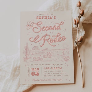 Könnte beinhalten: Eine rosafarbene und weiße Einladung zu einer zweiten Geburtstagsfeier mit Western-Thema. Die Einladung zeigt ein Lasso-Design mit den Worten "Sophia's Second Rodeo" und eine Comic-Zeichnung einer Wüstenlandschaft. Die Einladung enthält das Datum, die Uhrzeit und den Ort der Party.