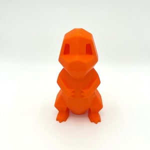 Puede incluir: Una figura geométrica de Charmander de color naranja brillante. La figura es de un solo color y tiene un diseño facetado. La figura está sobre una superficie blanca.