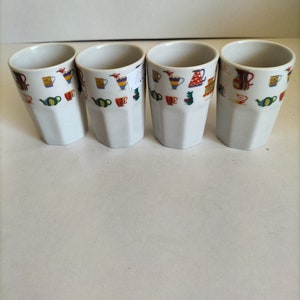 May include: Set of four white ceramic mugs featuring a colourful pattern of teapots, cups, and other tea-related items.