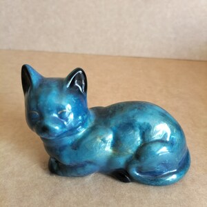 May include: A blue ceramic cat figurine with a glossy finish. The cat is lying down with its head resting on its paws.
