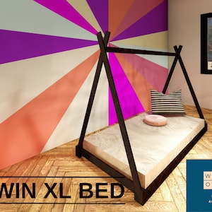 May include: A black wooden twin XL bed frame in a teepee style. The bed has a beige mattress, a striped pillow, and a round pink pillow. The wall behind the bed is painted with a colorful sunburst design. The text "TWIN XL BED" is at the bottom.