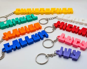 May include: A collection of 3D printed plastic keychains featuring names in block lettering. The names include Christopher in yellow, Samuel in teal, Xavier in orange, Callum in blue, Jerich in white, Michael in red, Lucy in pink, and Ivy in purple.