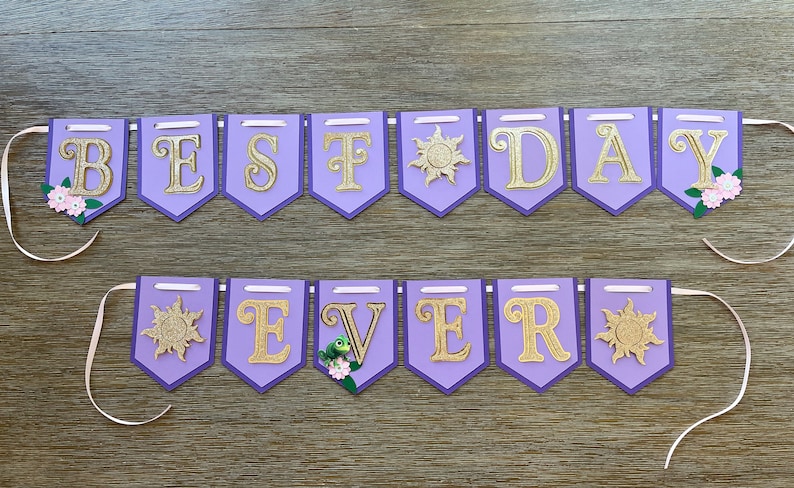 May include: A purple banner with gold glitter letters spelling "BEST DAY EVER". Each pennant has a gold border and is decorated with floral accents and sunburst designs. The banner is strung with white ribbon.