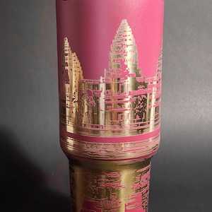 May include: A pink stainless steel travel mug with a gold-colored image of Angkor Wat, a temple complex in Cambodia.