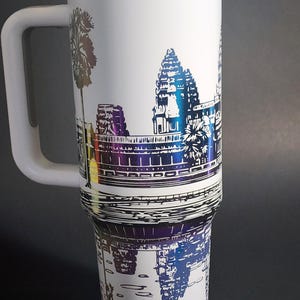 May include: White travel mug with a black and white image of Angkor Wat, a temple complex in Cambodia. The mug has a rainbow iridescent finish around the top.