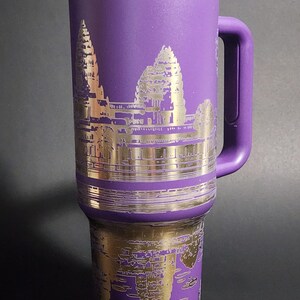 May include: Purple stainless steel travel mug with a gold-colored image of Angkor Wat temple on the front.