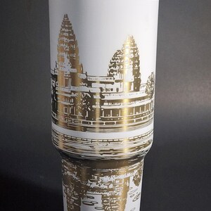 May include: White travel mug with a gold metallic design of Angkor Wat temple in Cambodia. The temple is depicted in a detailed silhouette.