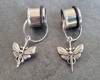 May include: A pair of silver ear gauges with a dangling skull and butterfly charm. The gauges are made of stainless steel and have a black rubber o-ring.